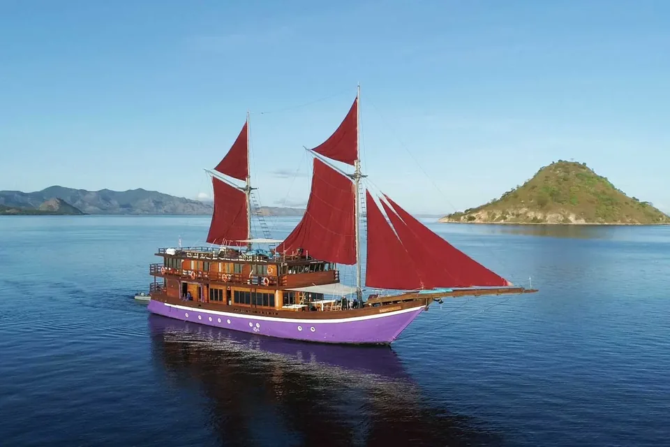 Phinisi liveaboard with red sails at anchor in Komodo waters